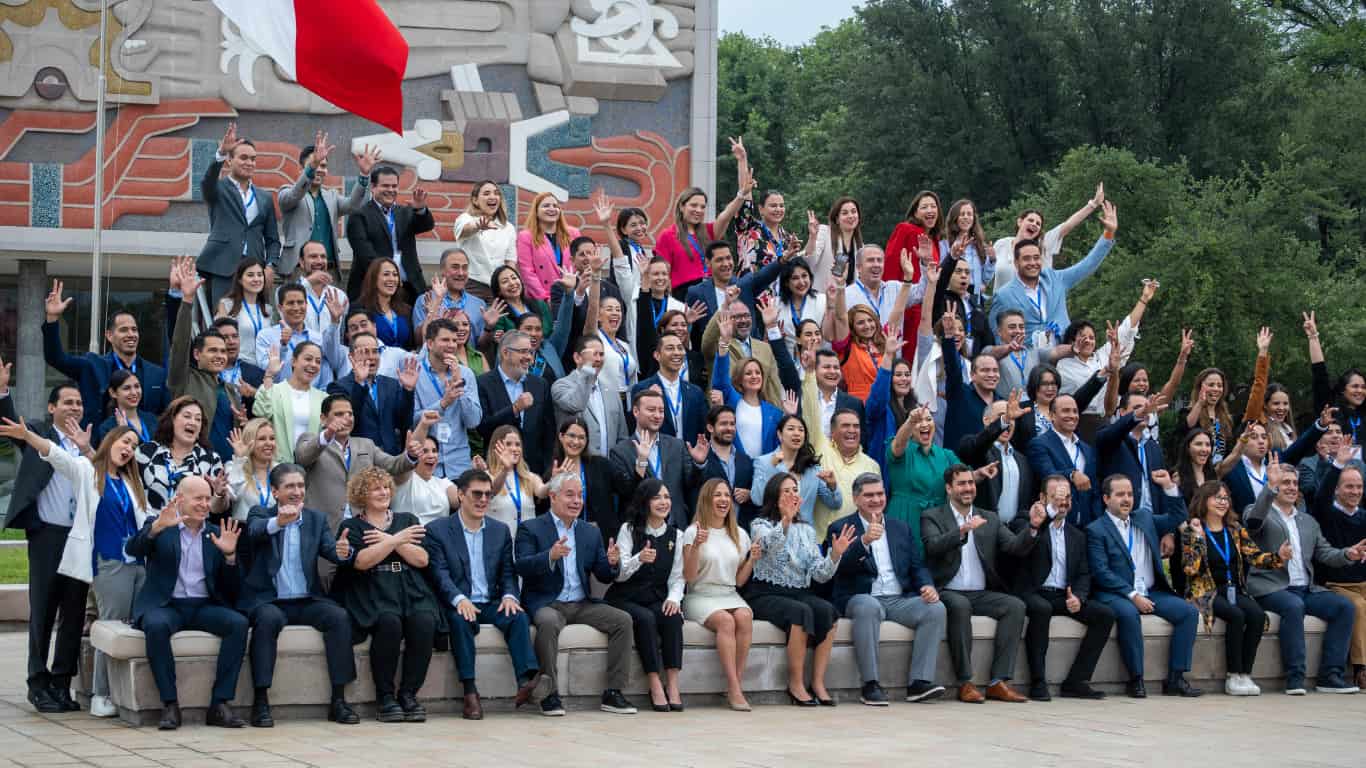 Foto grupal de representantes de asociaciones EXATEC de todo el mundo, reunidos frente al mural emblemático del Campus Monterrey durante la Reunión Anual de Presidencias EXATEC 2025. Todos posan sonriendo y levantando las manos en señal de celebración y unidad.