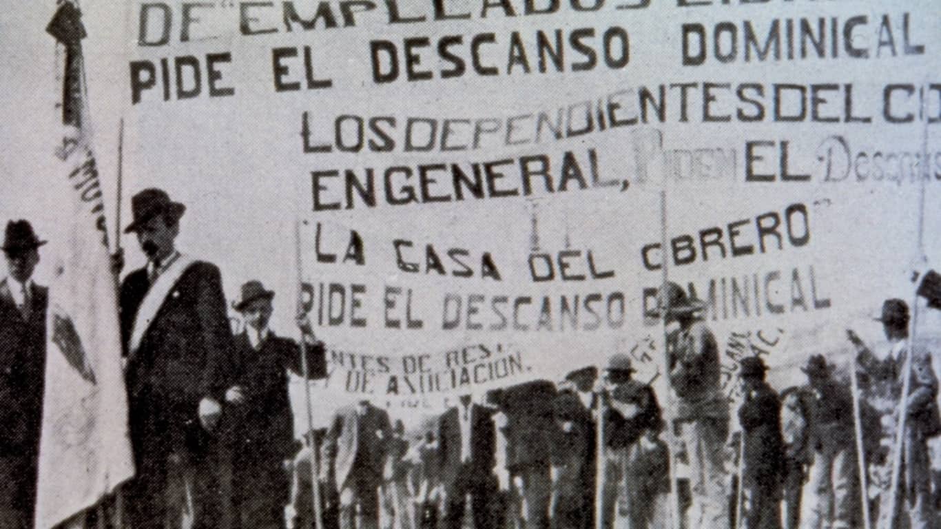 Una fotografía en blanco y negro de una manifestación histórica, con participantes sosteniendo pancartas que demandan el descanso dominical.