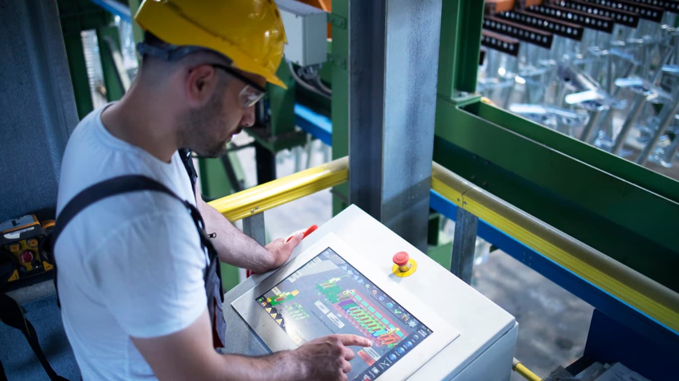 Un hombre con casco de seguridad y gafas protectoras está operando un panel de control en una instalación industrial.