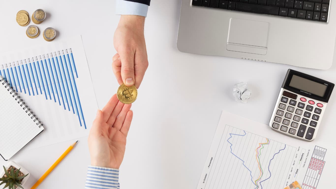 Una mano sostiene una moneda dorada con el símbolo de una criptomoneda, mientras otra mano está lista para recibirla.