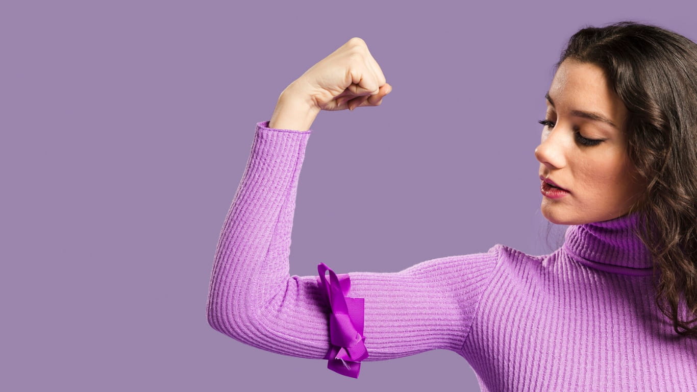 Una mujer con un suéter de cuello alto morado, mostrando su brazo flexionado en un gesto de fuerza.