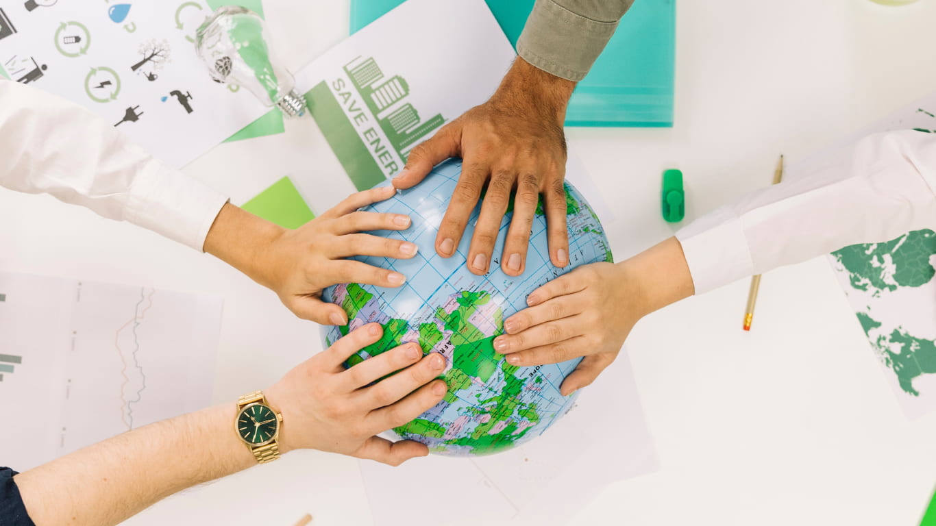 Varias manos de diferentes personas están unidas sobre un globo terráqueo, simbolizando la colaboración para el cuidado del medio ambiente.