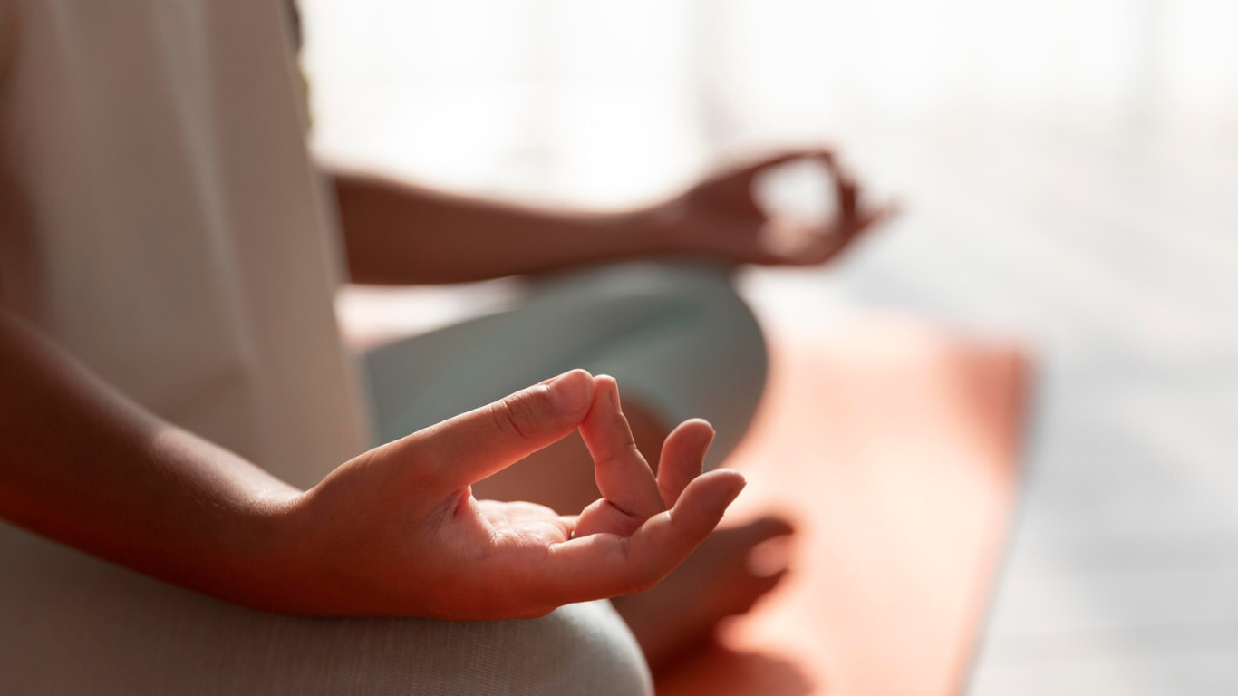 Primer plano de las manos de una persona en posición de meditación, haciendo un mudra con los dedos.
