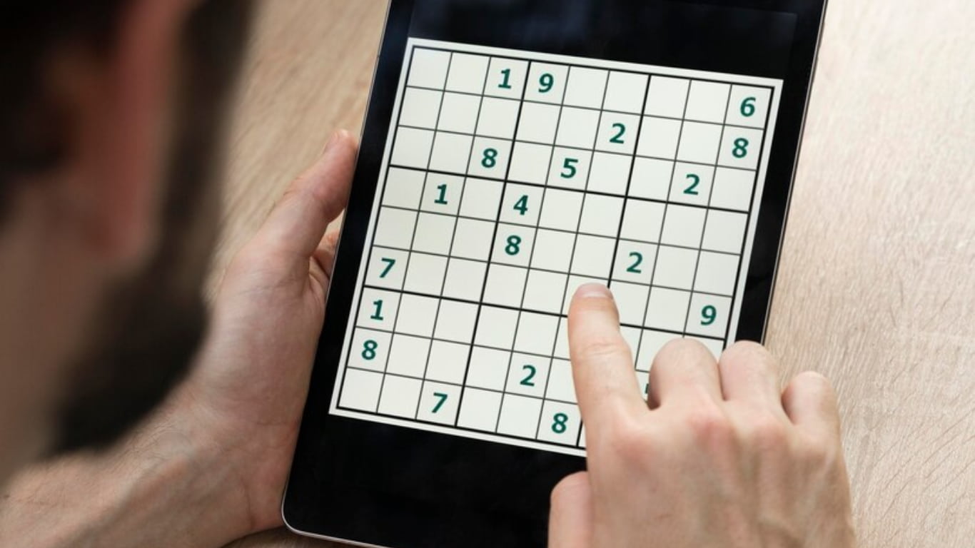Una hoja de papel con un puzzle de sudoku en una mesa de madera, junto a un bolígrafo negro y unas gafas.