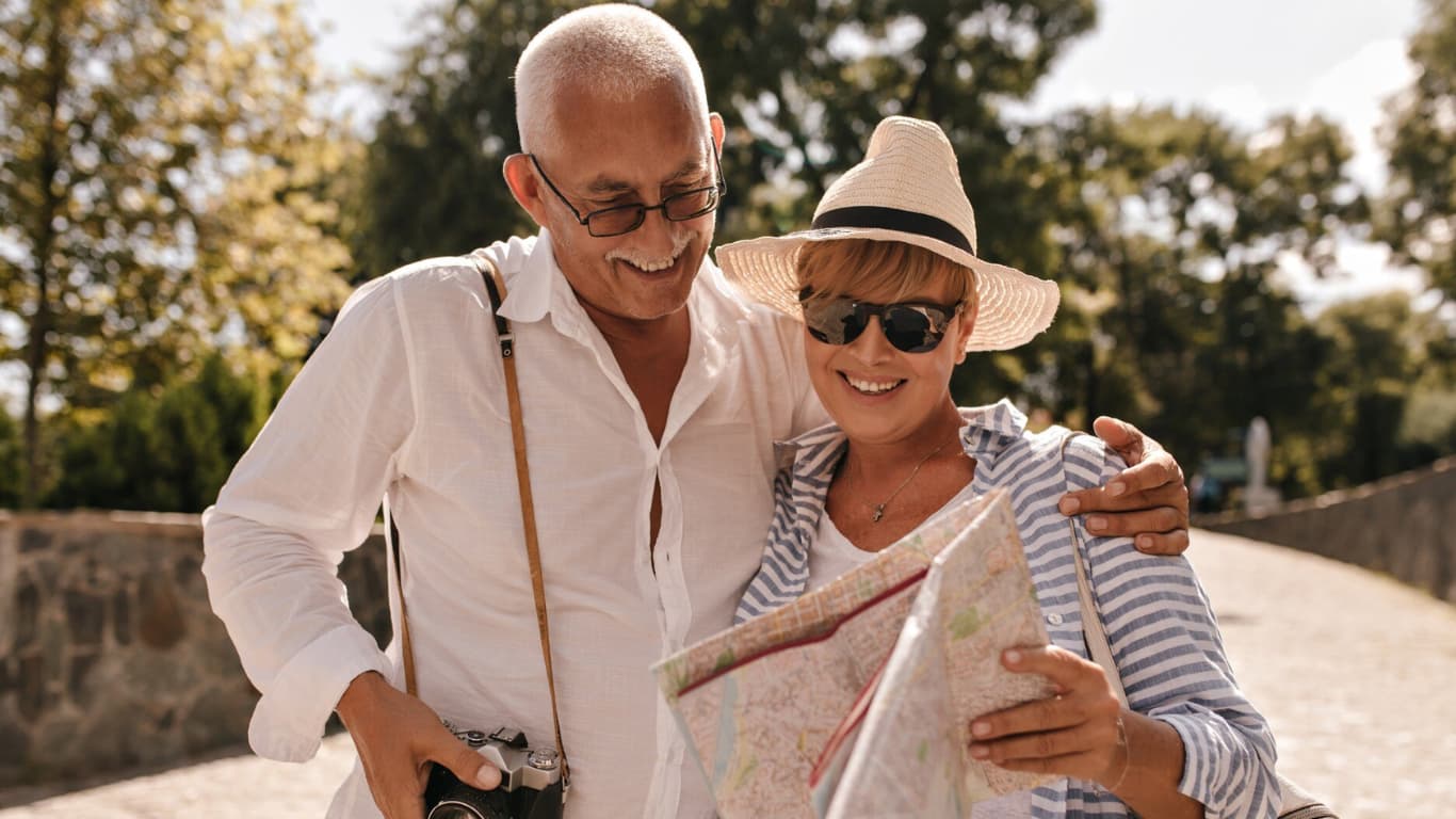 La misma pareja sonríe y se abrazan mientras miran un mapa juntos. El hombre sostiene una cámara colgada al cuello y la mujer, con un sombrero y gafas de sol, parece emocionada por su aventura.