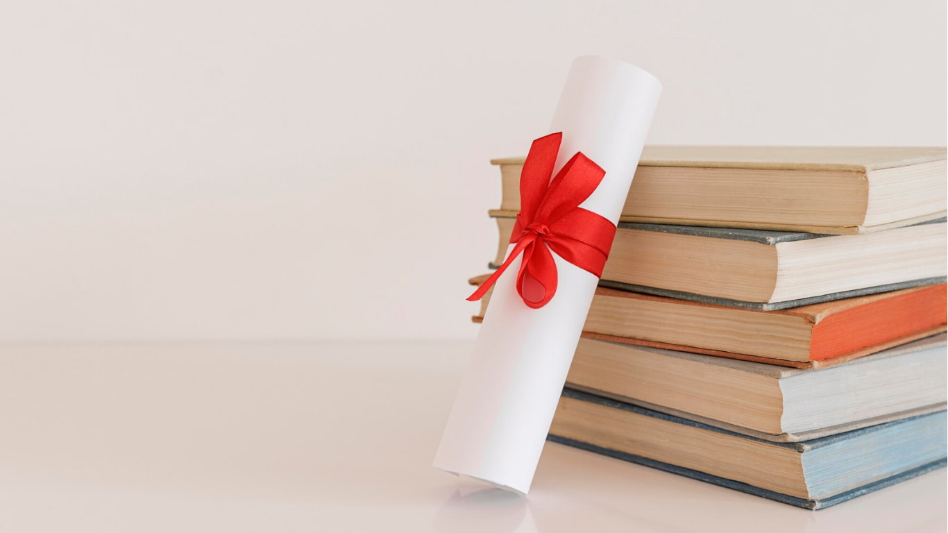 Un diploma enrollado con un lazo rojo descansa al lado de una pila de libros de diferentes colores.