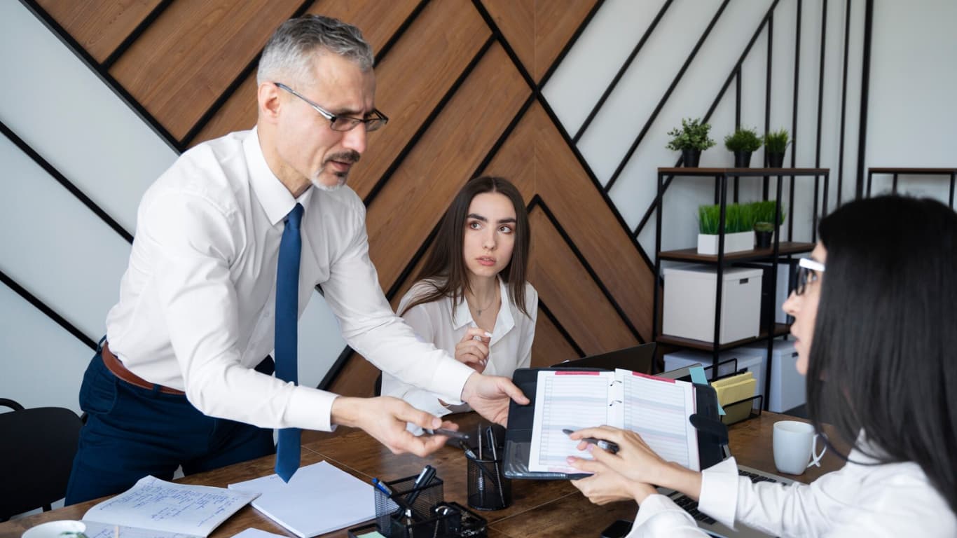 La escena muestra un ambiente de trabajo colaborativo, con un escritorio lleno de papeles y una decoración de diseño contemporáneo.