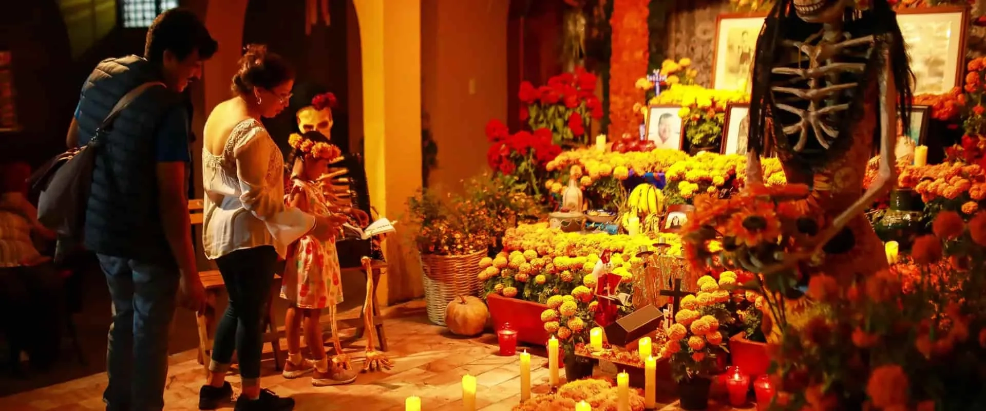 Una familia observa un altar decorado para el Día de los Muertos, con flores de cempasúchil y velas encendidas. 