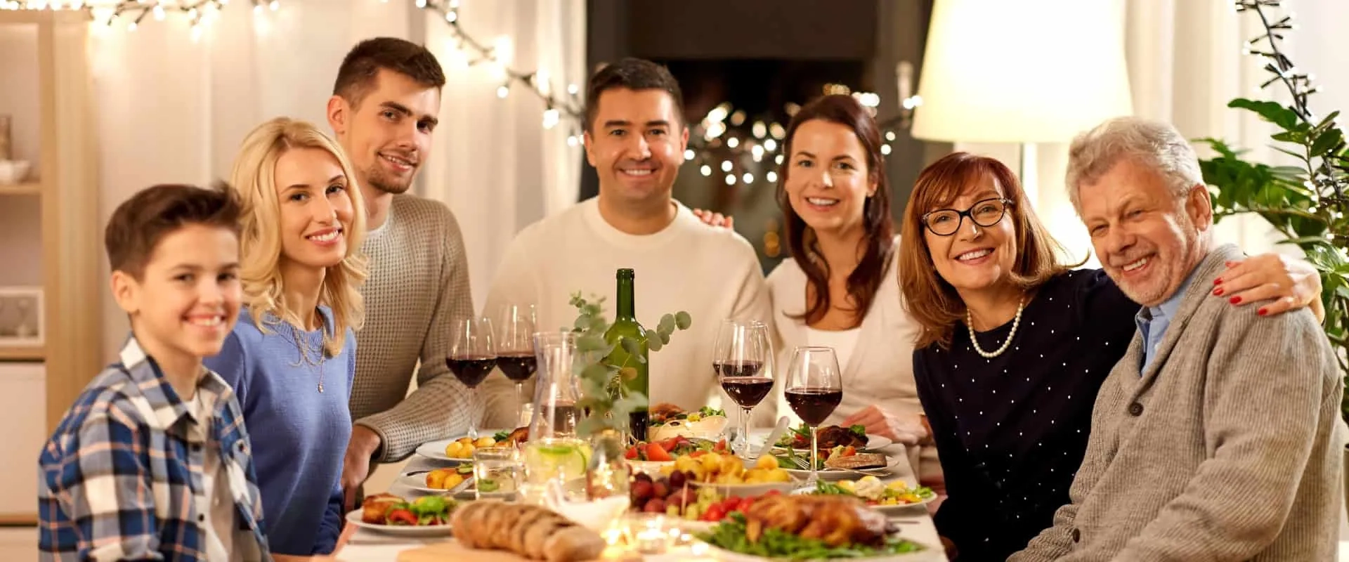 Un grupo de siete personas sonríe y posan para la foto en una mesa decorada con una cena abundante. Hay platos de comida variada, copas de vino y botellas en la mesa.