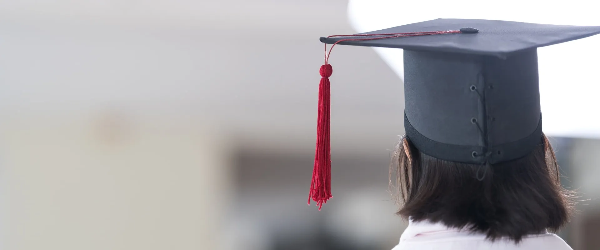 Una vista posterior de una persona con un birrete de graduación negro, que tiene una borla roja.