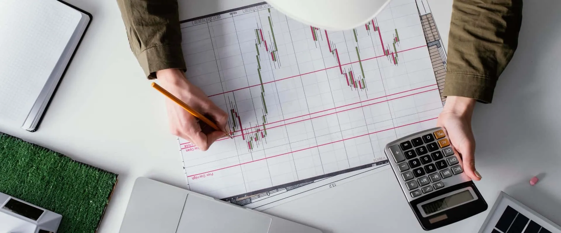 Una persona trabaja en un gráfico financiero, utilizando un lápiz para marcar datos en un papel con líneas de gráficos de velas. 