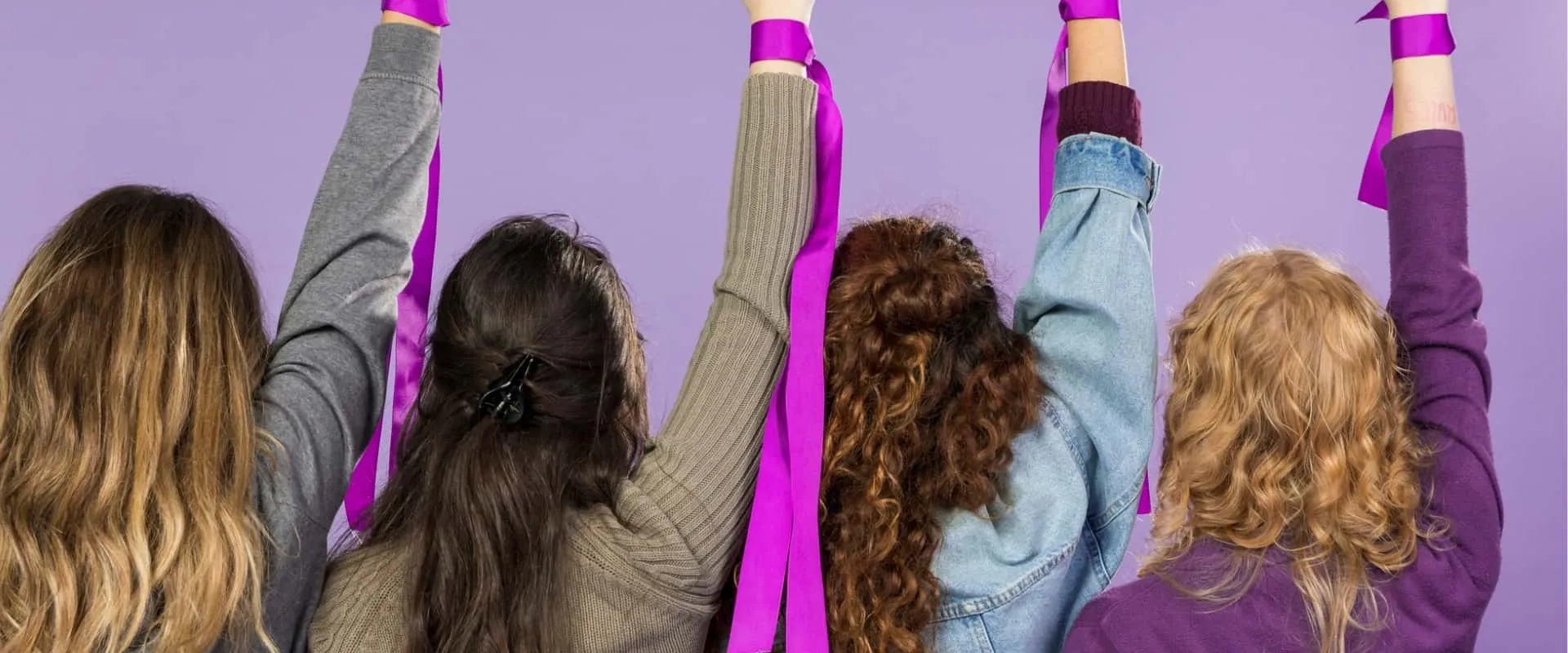 Cinco mujeres de espaldas levantando cintas moradas en un fondo morado. Sus cabellos tienen diferentes estilos y colores, y la imagen transmite una sensación de celebración y unidad.