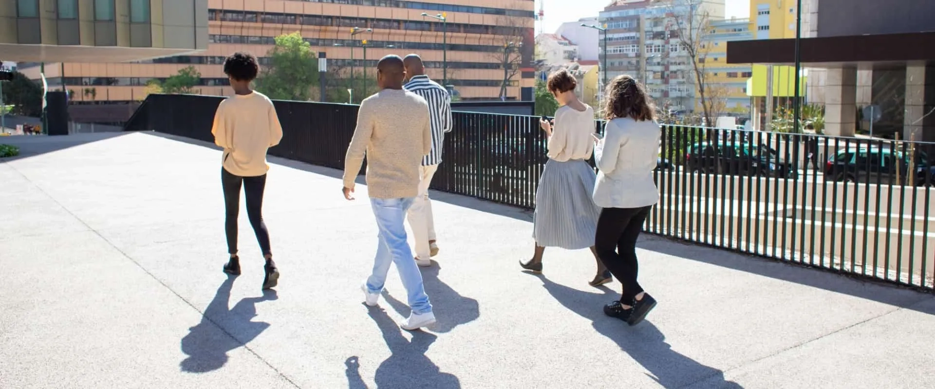 Un grupo de cinco personas caminando juntas por un área urbana. Todos llevan ropa casual y están de espaldas, dirigiéndose hacia un destino común.