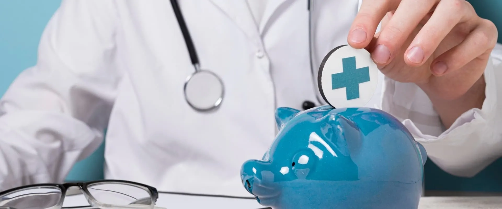 Un médico con un estetoscopio alrededor del cuello está insertando una moneda con un símbolo de cruz en una alcancía en forma de cerdo azul.