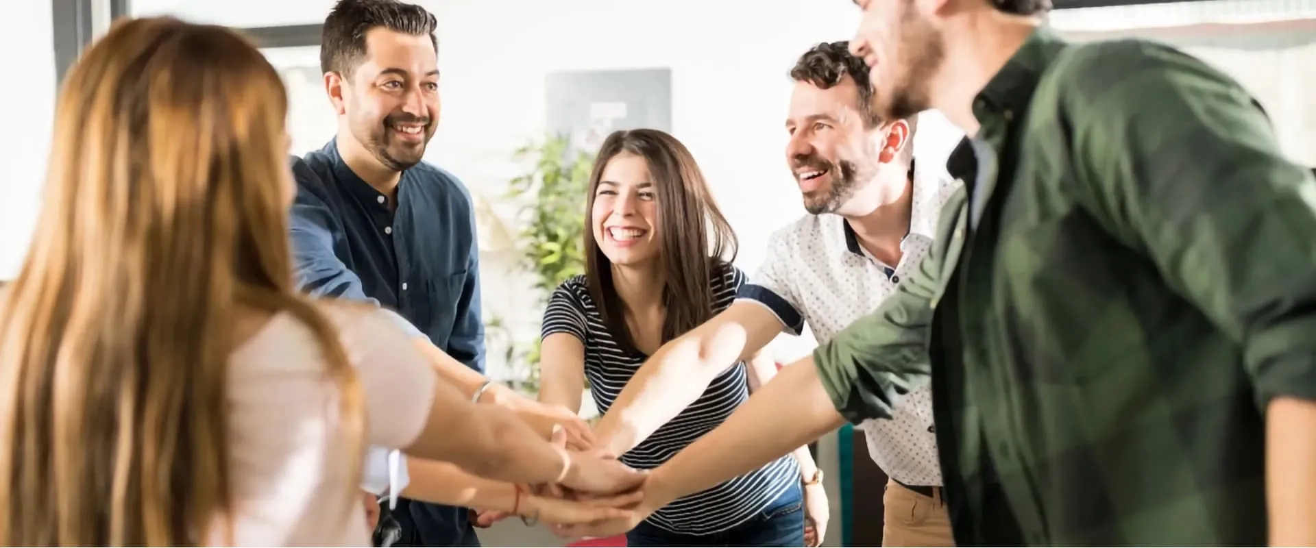 Un grupo de cinco personas sonrientes se reúne en un círculo, con las manos unidas en el centro en señal de celebración o apoyo.