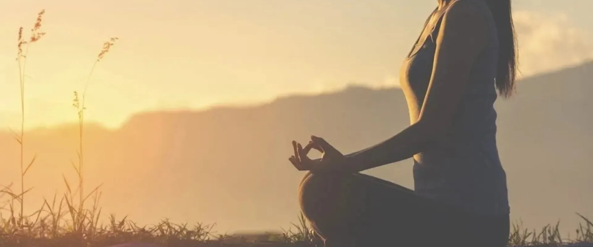 Una mujer está sentada en posición de meditación al aire libre, con las piernas cruzadas y las manos en posición de mudra.