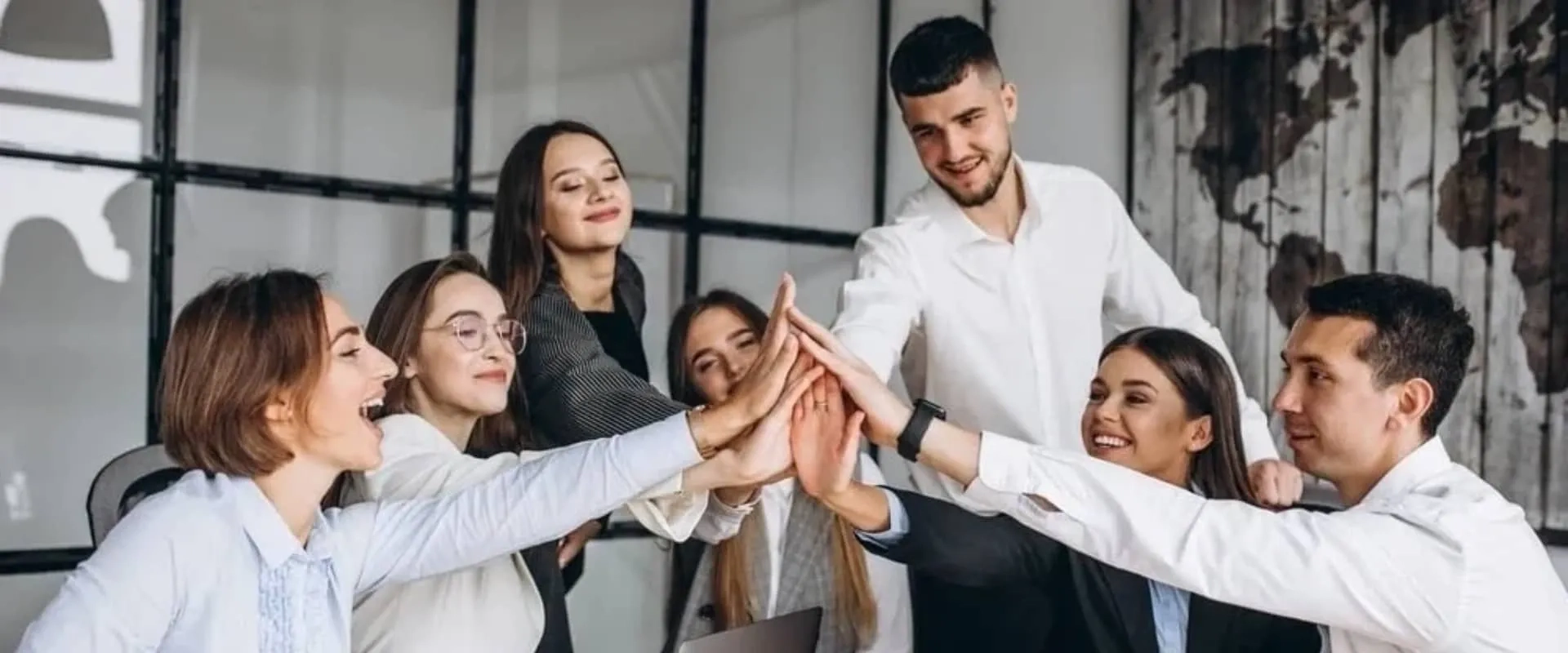 Un grupo de seis personas en un entorno de oficina se reúne para una sesión de team building. Están levantando las manos y chocando palmas en un gesto de celebración y camaradería.