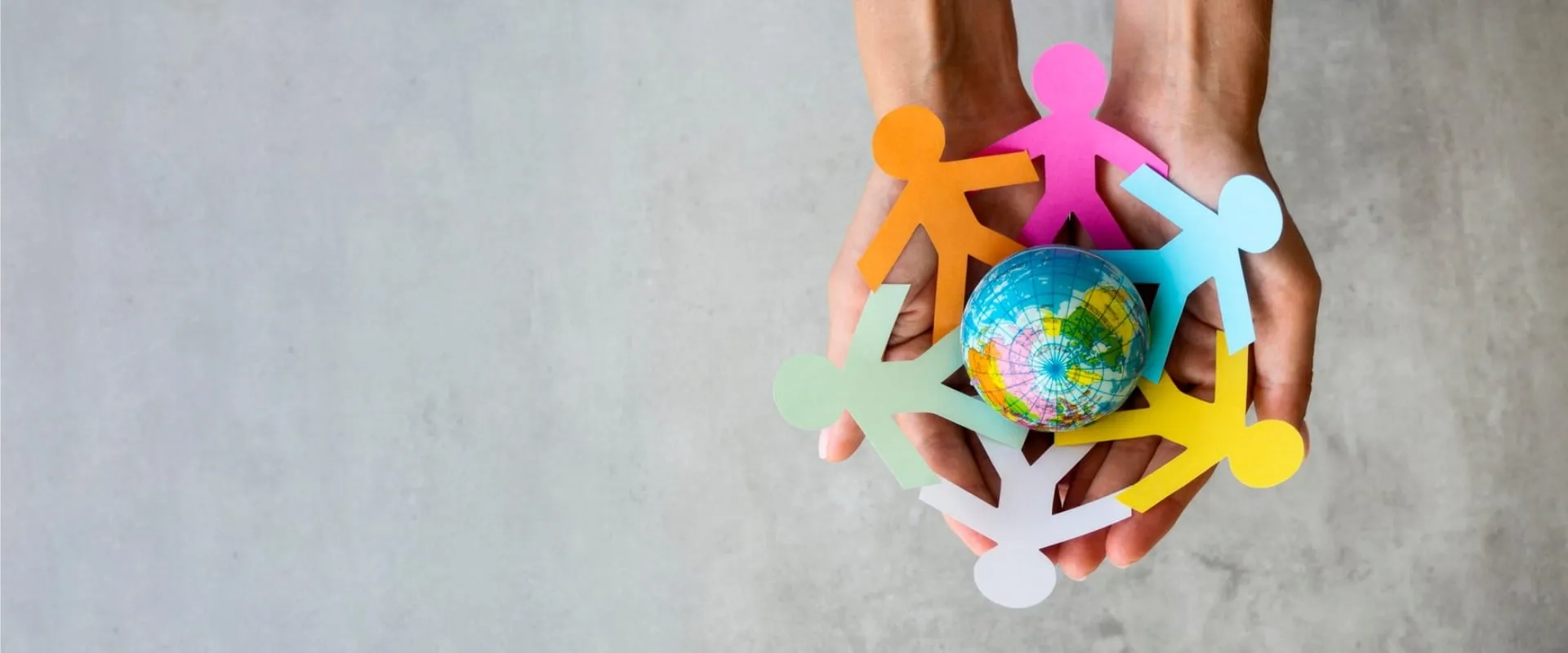 Manos sosteniendo un globo terráqueo rodeado de figuras de papel en colores brillantes que representan personas.