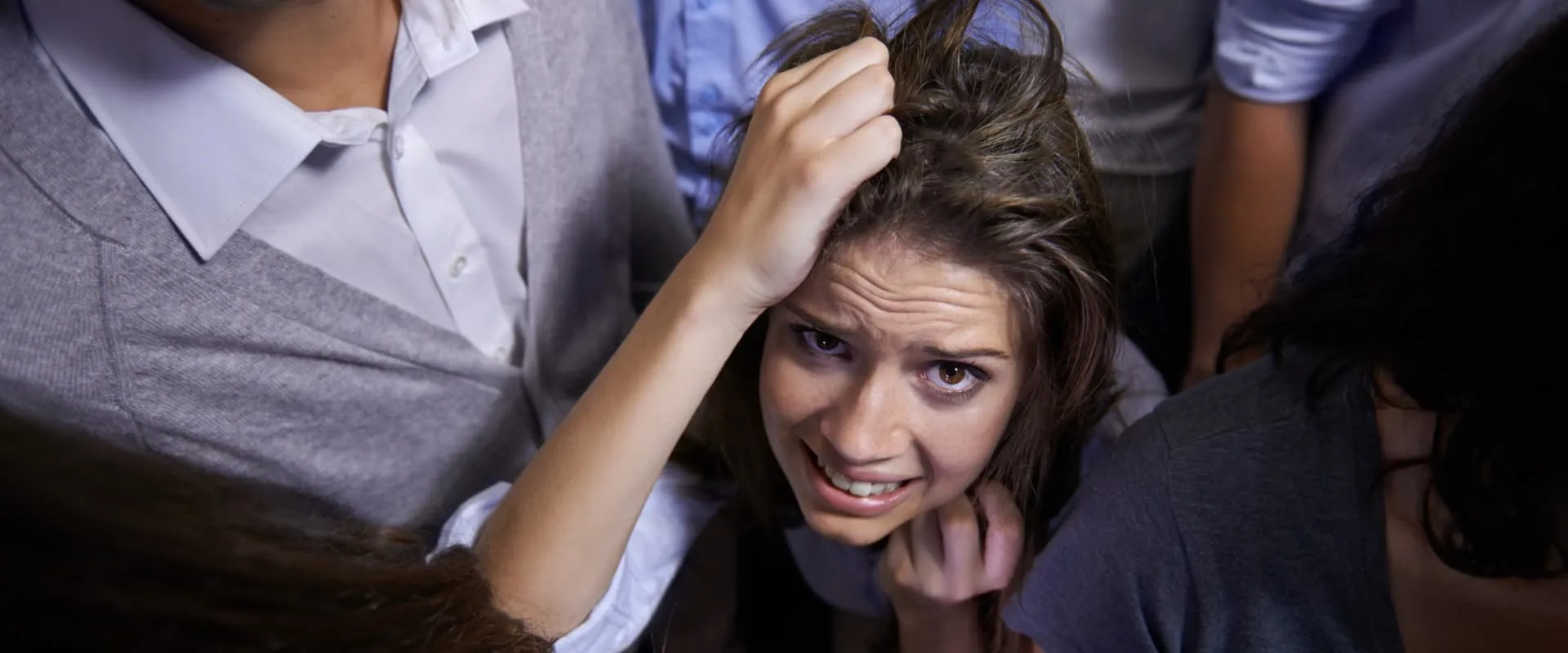 Un primer plano de una mujer con expresión angustiada, rodeada de personas. Su cabello está desarreglado y parece estresada, mientras las manos de la multitud son visibles alrededor de ella. La imagen transmite una sensación de agobio y ansiedad en un entorno abarrotado.