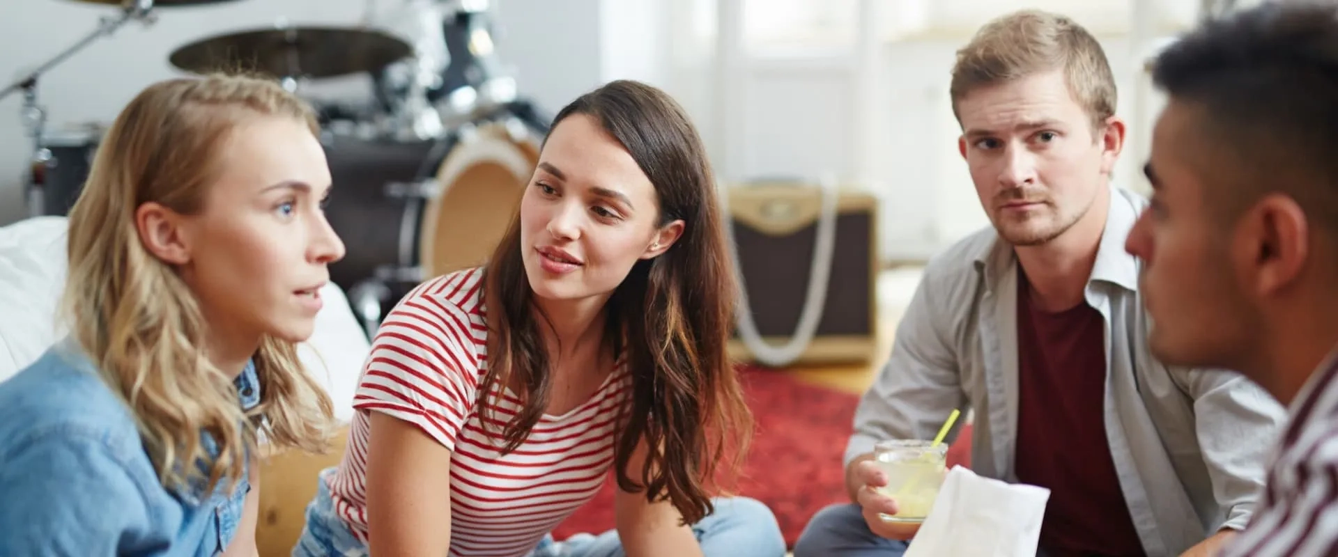 Un grupo de cuatro amigos sentados en un ambiente acogedor, conversando animadamente. Dos mujeres y dos hombres están atentos a la conversación, mostrando interés y sonrisas.