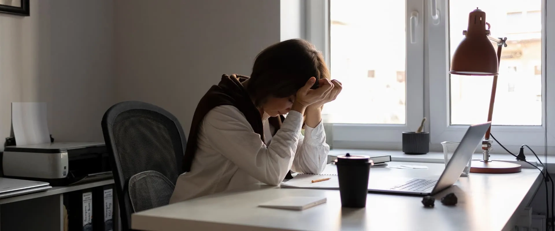 Mujer joven con señales de estrés laboral frente a una computadora portátil en oficina, representando la importancia de la salud mental en el trabajo.