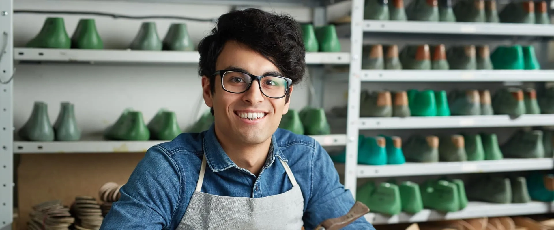 Joven emprendedor sonriente en taller de calzado artesanal, representando el espíritu del emprendimiento y la innovación en la industria manufacturera.