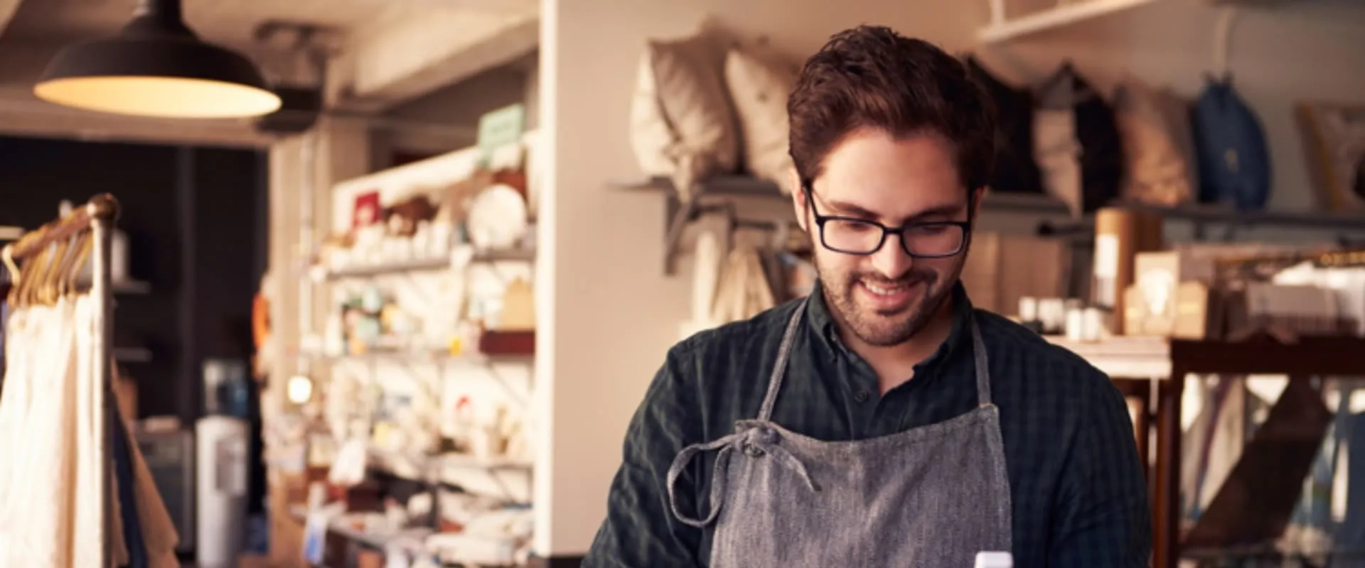 Emprendedor joven atendiendo su tienda con entusiasmo, rodeado de productos artesanales, como ejemplo de negocio independiente con bajo presupuesto.
