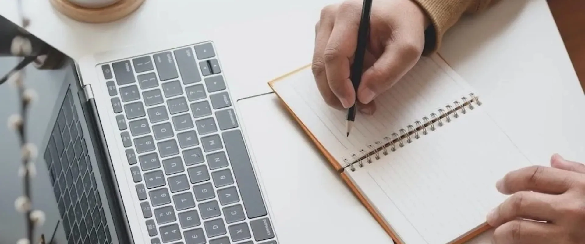 Estudiante tomando notas a mano mientras estudia en línea con su laptop, en un entorno de aprendizaje remoto.