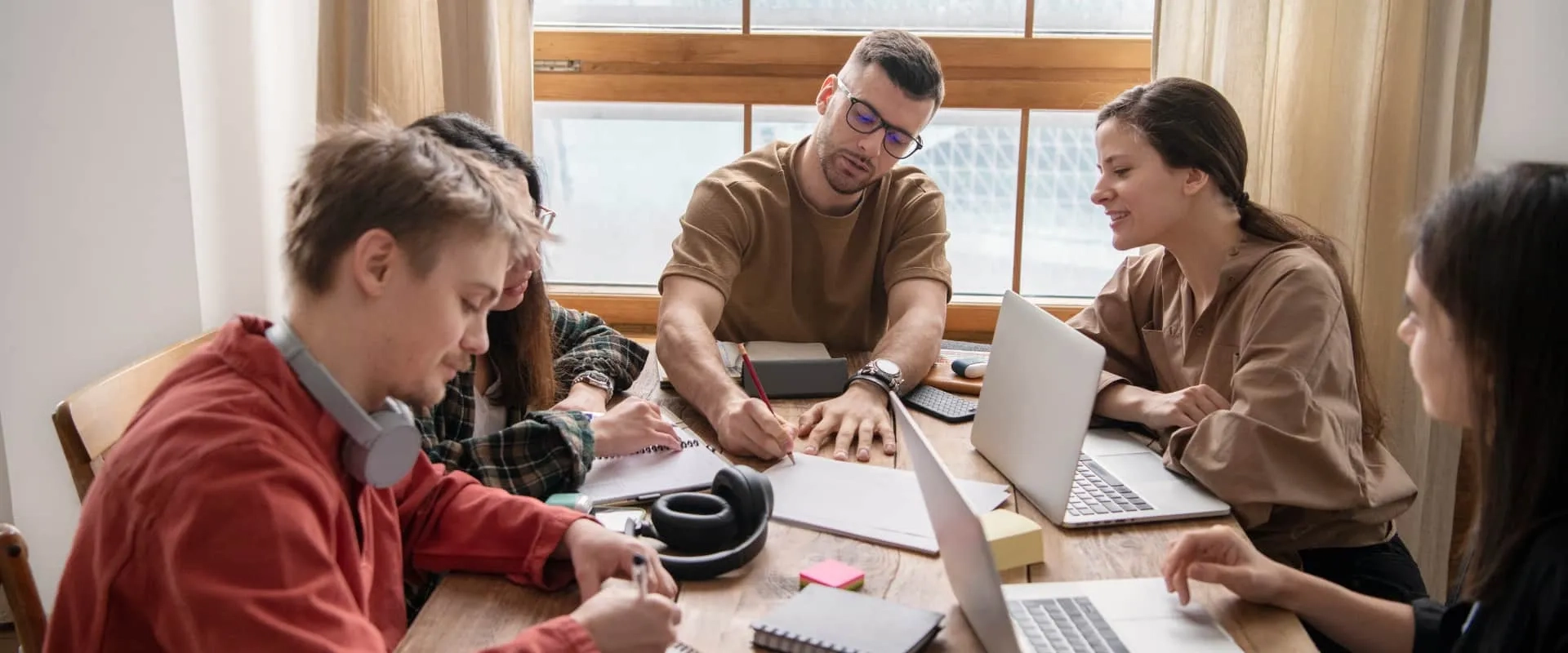 Grupo de jóvenes colaborando en proyecto creativo con laptops y cuadernos, durante sesión práctica de storytelling profesional.