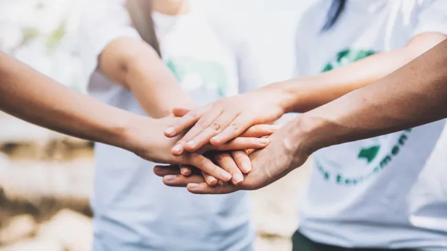 Manos de egresados EXATEC unidas sobre otra, simbolizando el trabajo en equipo, la colaboración y el voluntariado profesional de la comunidad.